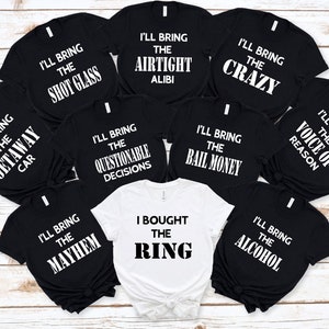 May include: Nine black t-shirts with white text, each with a different phrase related to a wedding. One white t-shirt with black text that says "I bought the ring".