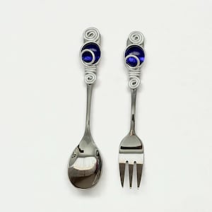 May include: A set of silverware with blue glass beads on the handles. The spoon and fork are made of silver and have a polished finish.