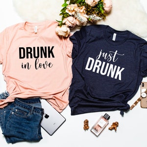 May include: Two t-shirts with a matching design. One shirt is pink with black text that says "DRUNK in love". The other shirt is navy blue with white text that says "just DRUNK".