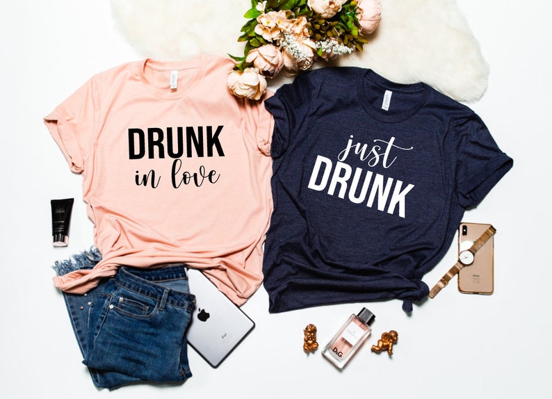May include: Two t-shirts with a matching design. One shirt is pink with black text that says "DRUNK in love". The other shirt is navy blue with white text that says "just DRUNK".