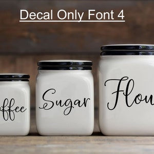 May include: Three white ceramic canisters with black lids and black vinyl lettering. The canisters are labeled "Coffee", "Sugar", and "Flour" in a cursive font.