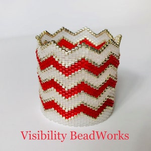 May include: A red and white beaded bracelet with a chevron pattern. The bracelet is made with small, round beads and has a gold trim.