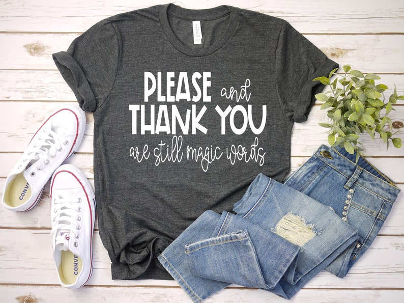 May include: A dark gray t-shirt with the text "PLEASE and THANK YOU are still magic words" printed in white.