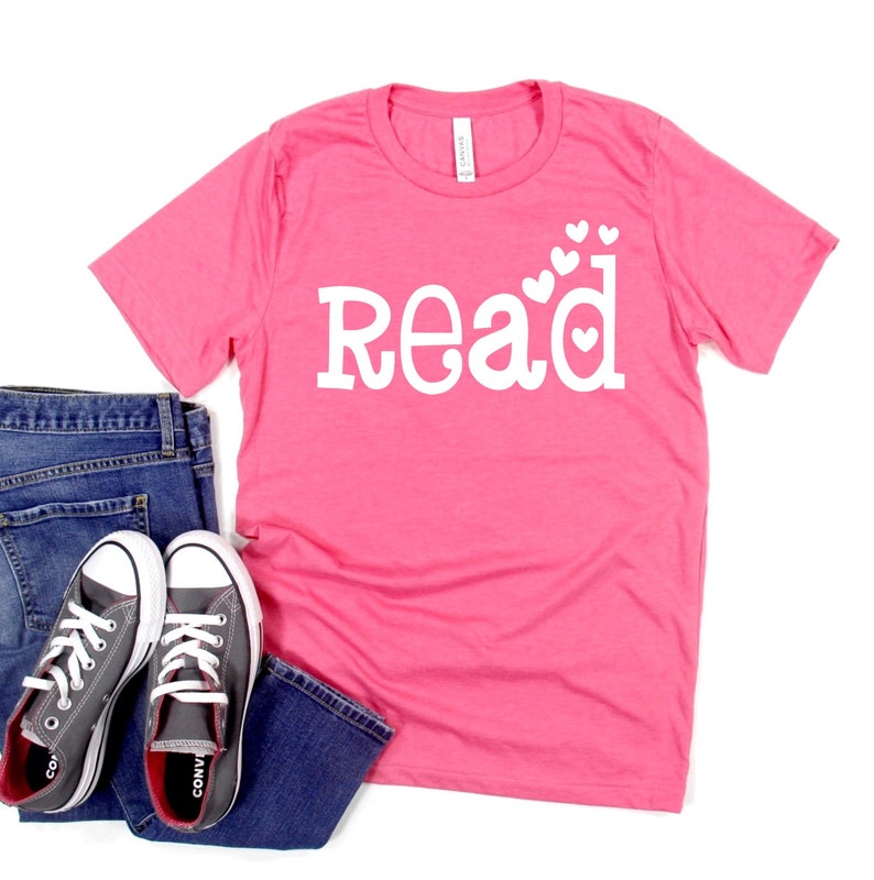 May include: Pink t-shirt with white text that says "Read" with small white hearts around the letters.