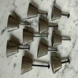 May include: A set of nine metallic cabinet knobs, each featuring a smooth, truncated cone shape with a polished silver-tone finish. Every knob includes a threaded metal screw extending from the center of the flat base for installation purposes.