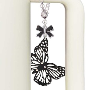 May include: Black metal butterfly charm with a black bow and a silver chain. The charm is attached to a white thermos.