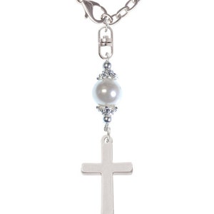 May include: A silver charm necklace with a white pearl, a silver cross, and a silver disc with the letter 'A' on it.