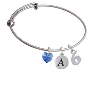 May include: A silver bangle bracelet with three charms: a blue crystal heart, a round charm with the letter "A" and a charm with the number "6".