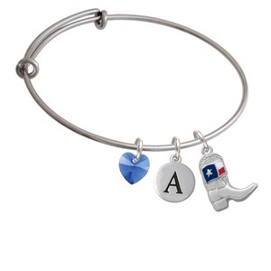 May include: Silver-toned adjustable bangle bracelet with three charms. Charms include a blue heart-shaped crystal, a round disc with the letter "A", and a cowboy boot with a Texas flag design. The bracelet is a stylish accessory.