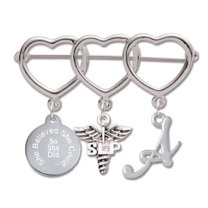 May include: Silver charm bracelet with three heart-shaped charms. The charms are connected by a silver chain. The charms have a silver medical symbol, a silver letter A, and a silver charm with the text "She Believed She Could So She Did..."