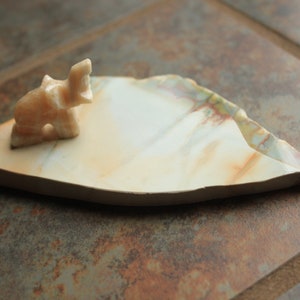 May include: A small, white, carved elephant figurine sits on a white, irregularly shaped, stone dish with brown and green marbling.