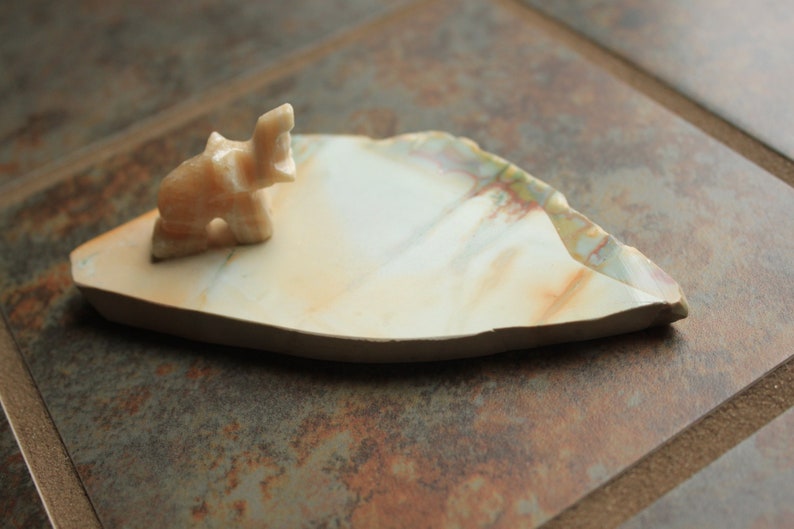 May include: A small, white, carved elephant figurine sits on a white, irregularly shaped, stone dish with brown and green marbling.