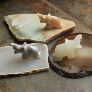 May include: Three small white elephant figurines on different natural stone bases. The elephants are carved from white marble and are in various poses. The bases are made of agate, jasper, and a white stone.