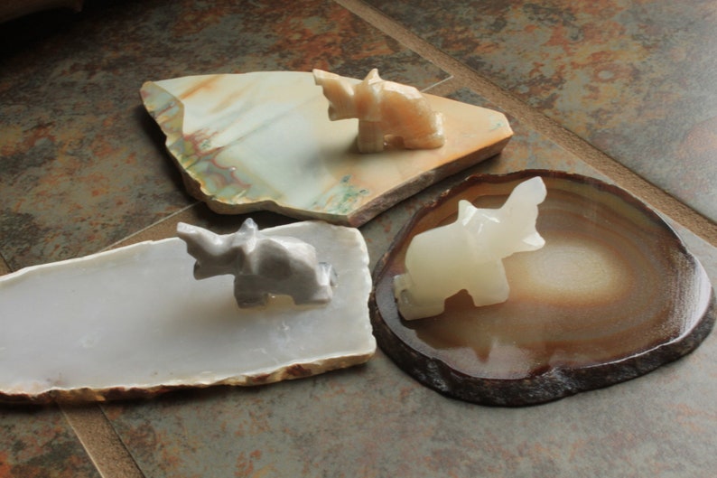 May include: Three small white elephant figurines on different natural stone bases. The elephants are carved from white marble and are in various poses. The bases are made of agate, jasper, and a white stone.