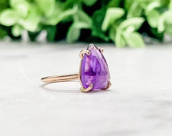May include: A pear-shaped amethyst gemstone ring set in rose gold. The ring features a prong setting and a deep purple amethyst.