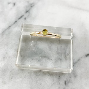 May include: A delicate gold ring with a small, round, light green gemstone set in the center.