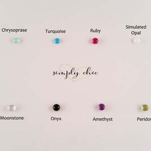 May include: A collection of small, round gemstones in various colors, including turquoise, ruby, and amethyst, are displayed on a white surface. The gemstones are labeled with their names, such as "Amazonite" and "Lapis Lazuli." The words "simply chic" are written in cursive.