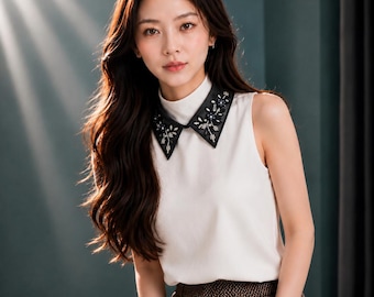 May include: A sleeveless white top featuring a high mock neck and a contrasting black pointed collar. The collar is embellished with intricate floral embroidery in shades of blue, silver, and black, paired with brown textured trousers.