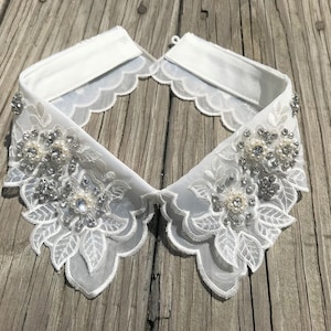 May include: White lace collar with a scalloped edge and embellished with silver and pearl-like beads.