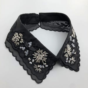 May include: A black faux-fur collar with a scalloped edge and silver and black beaded embellishments in a floral pattern.