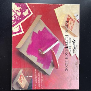 May include: A Speedball dual-purpose inking plate and bench hook for block printing. The box is red with a pink inking area and a red roller. The text on the box reads "INKING PLATE/BENCH HOOK".