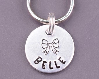 May include: Silver dog tag with a bow and the name "BELLE" engraved on it.