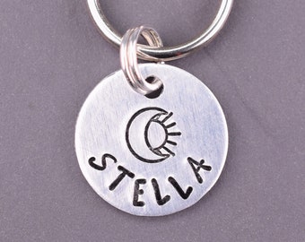 May include: Silver key ring with a round tag that says "STELLA" with a moon and sun design.
