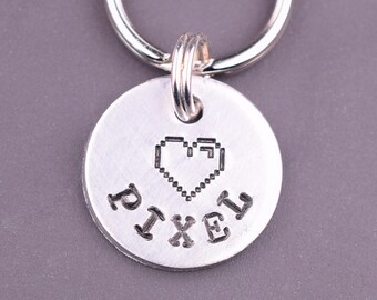 May include: Silver key chain with a round tag that says "PIXEL" and has a pixelated heart design.