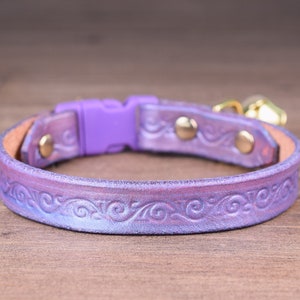 Peut inclure: Un collier pour chat en cuir violet avec un motif gaufré décoratif et une boucle en plastique violette. Le collier a deux breloques de cloche dorées.