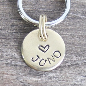 May include: Gold-toned keychain with a round tag that says "JUNO" with a heart symbol above the name.