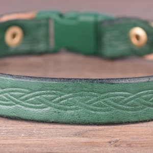 May include: A green leather dog collar featuring a Celtic knot pattern. The collar has a buckle fastening and brass-coloured rivets. The inside of the collar is a lighter tan colour.