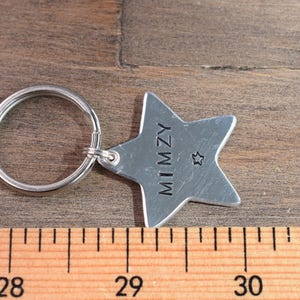 May include: Silver star-shaped keychain with the name "MIMZY" engraved on it. The keychain has a small star charm and a silver ring.