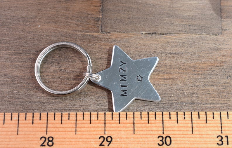 May include: Silver star-shaped keychain with the name "MIMZY" engraved on it. The keychain has a small star charm and a silver ring.