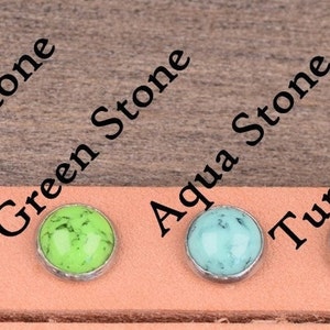 Puede incluir: Una selecci&oacute;n de cabujones de piedra de colores: rojo, naranja, blanco, verde, turquesa, morado y negro, cada uno engastado en un bisel plateado. Las piedras se muestran sobre una tira de cuero marr&oacute;n claro, con los nombres de las piedras impresos.