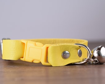 May include: A yellow leather cat collar with a silver buckle and a silver bell.