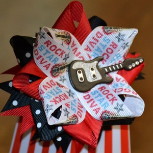 May include: A white, red, and black hair bow with a guitar and the words "Rock Star Diva" printed on it.