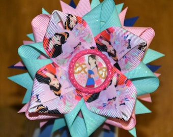 May include: A pink, blue, and white bow with a glittery finish. The bow features a round, pink button with a picture of a princess in a blue and red dress. The button has a gold design around the edge.