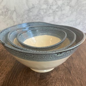 May include: A set of three nesting bowls with a speckled blue and white glaze. The bowls are made of ceramic and have a rounded shape.