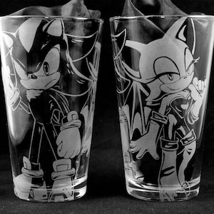 May include: Two clear glass pint glasses with etched designs of Shadow the Hedgehog and Rouge the Bat from the Sonic the Hedgehog video game series.