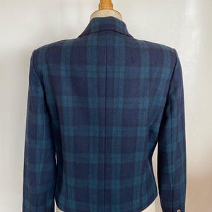 May include: A navy blue and teal plaid blazer displayed on a mannequin. The blazer has a classic plaid pattern, a notched collar, and three gold buttons on each cuff. The back of the blazer is visible, showcasing the tailored fit and design.
