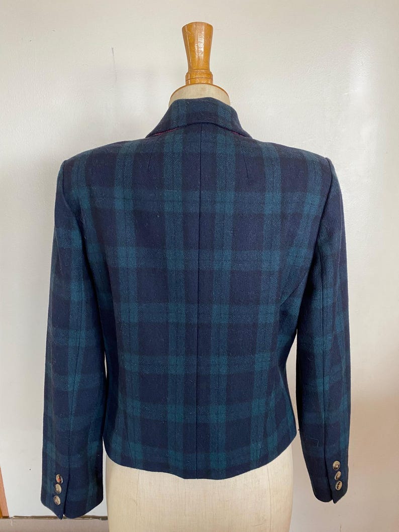May include: A navy blue and teal plaid blazer displayed on a mannequin. The blazer has a classic plaid pattern, a notched collar, and three gold buttons on each cuff. The back of the blazer is visible, showcasing the tailored fit and design.
