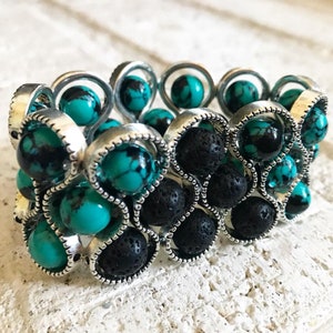 Könnte beinhalten: Ein dehnbares Armband mit türkisfarbenen und schwarzen Perlen. Die Perlen sind in silberfarbenem Metall gefasst.