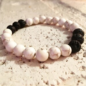 Può includere: Un braccialetto di perline bianche e nere con perline di lava. Il braccialetto è fatto di perline bianche di howlite e perline nere di lava.