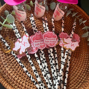 May include: A set of 10 black and white striped paper straws with pink and gold cowgirl themed toppers. The toppers feature the text "Let's Go Girls!" and "Hannah's Last Rodeo".