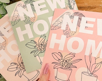 May include: Three greeting cards with the words "NEW HOME" in white block letters. Each card features a different pastel color: light pink, light green, and pink. The cards have illustrations of plants and leaves.