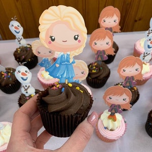 Könnte beinhalten: Schokoladen-Cupcakes, verziert mit bunten Streuseln und mit Frozen-Charakter-Toppern. Die Topper sind Elsa, Anna und Olaf.