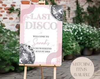 May include: A pink and white welcome sign with the text "Last Disco" and "Welcome to Sarah's Hen Do Weekend 3rd August 2024". The sign features a silver disco ball and pink and white stripes.