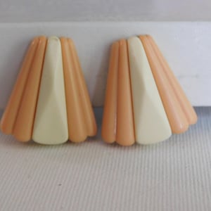 May include: A pair of peach and white plastic earrings with a fan-shaped design.