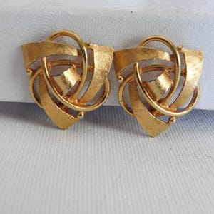 May include: A pair of gold-toned geometric earrings with a modern design. The earrings are made of metal and have a textured finish.