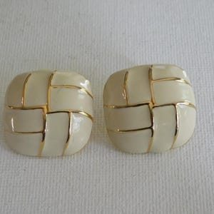 May include: A pair of square, cream-colored clip-on earrings with a gold-tone grid design. The earrings have a glossy finish and a vintage aesthetic, suitable for adding a touch of elegance to any outfit.